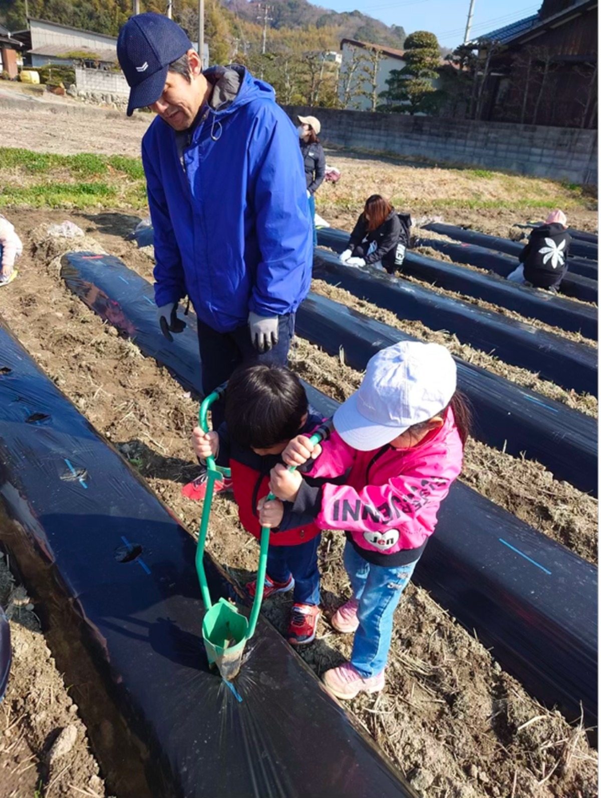 苗を植える子ども2人と見守る大人の写真